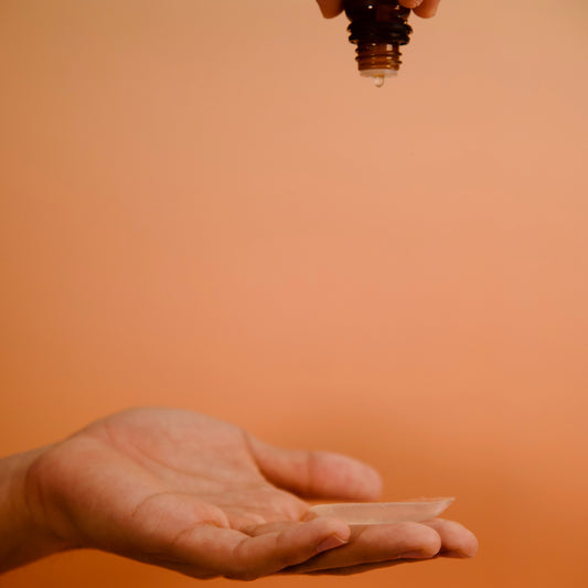 Hand holding a small container above another hand on an orange background